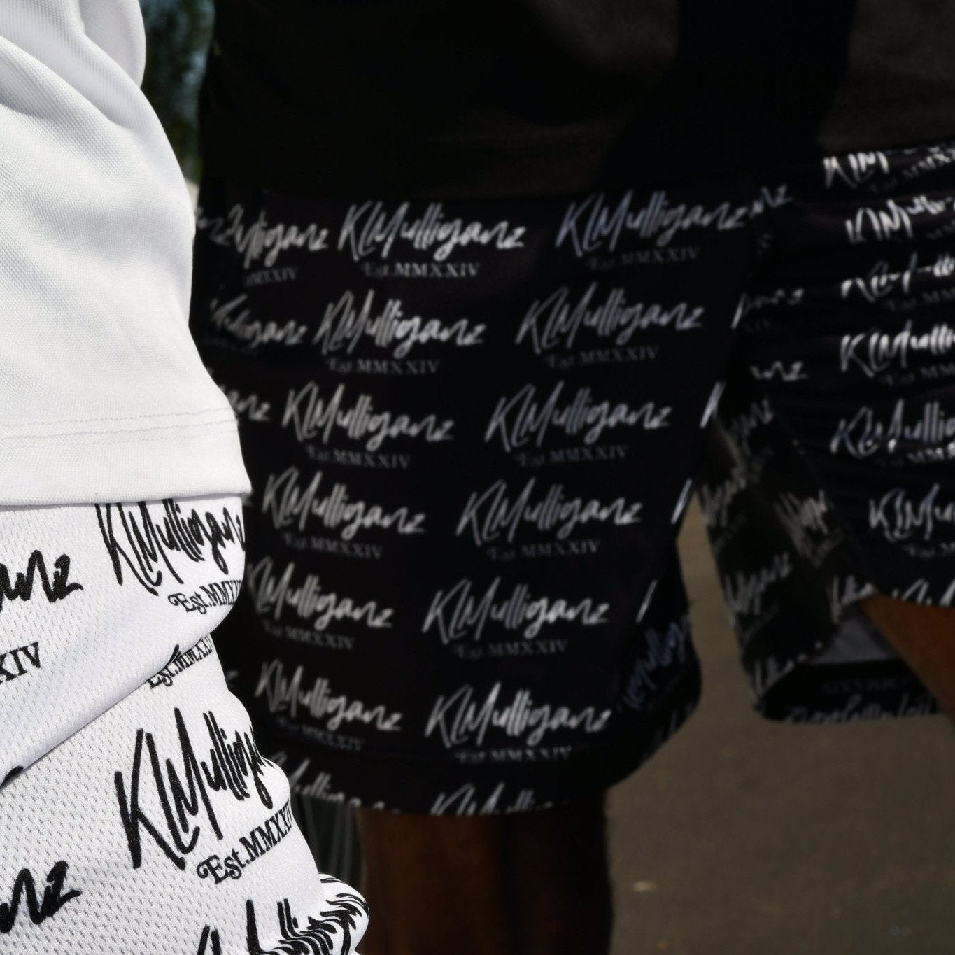 A close-up image highlighting the Legacy Shorts from KLMulliganz in both white and black variations. The shorts feature a dynamic all-over print of the “KLMulliganz” logo, representing the brand’s unique blend of golf fashion and lifestyle wear. The image captures the contrast between the two color options, emphasizing the versatility and style that these signature shorts bring to both the golf course and casual settings. The Legacy Shorts are designed for comfort and performance.